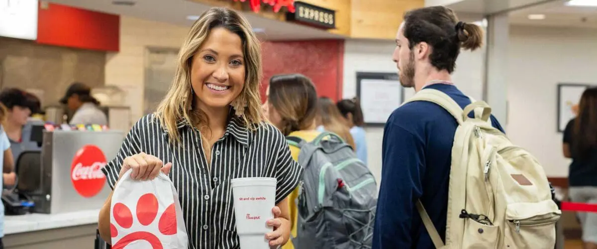 Woman smiling while holding a Chick-fil-A bag and beverage in front of counter
