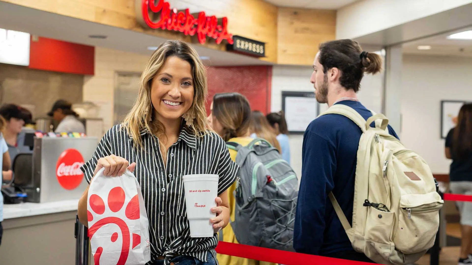 Woman smiling while holding a Chick-fil-A bag and beverage in front of counter