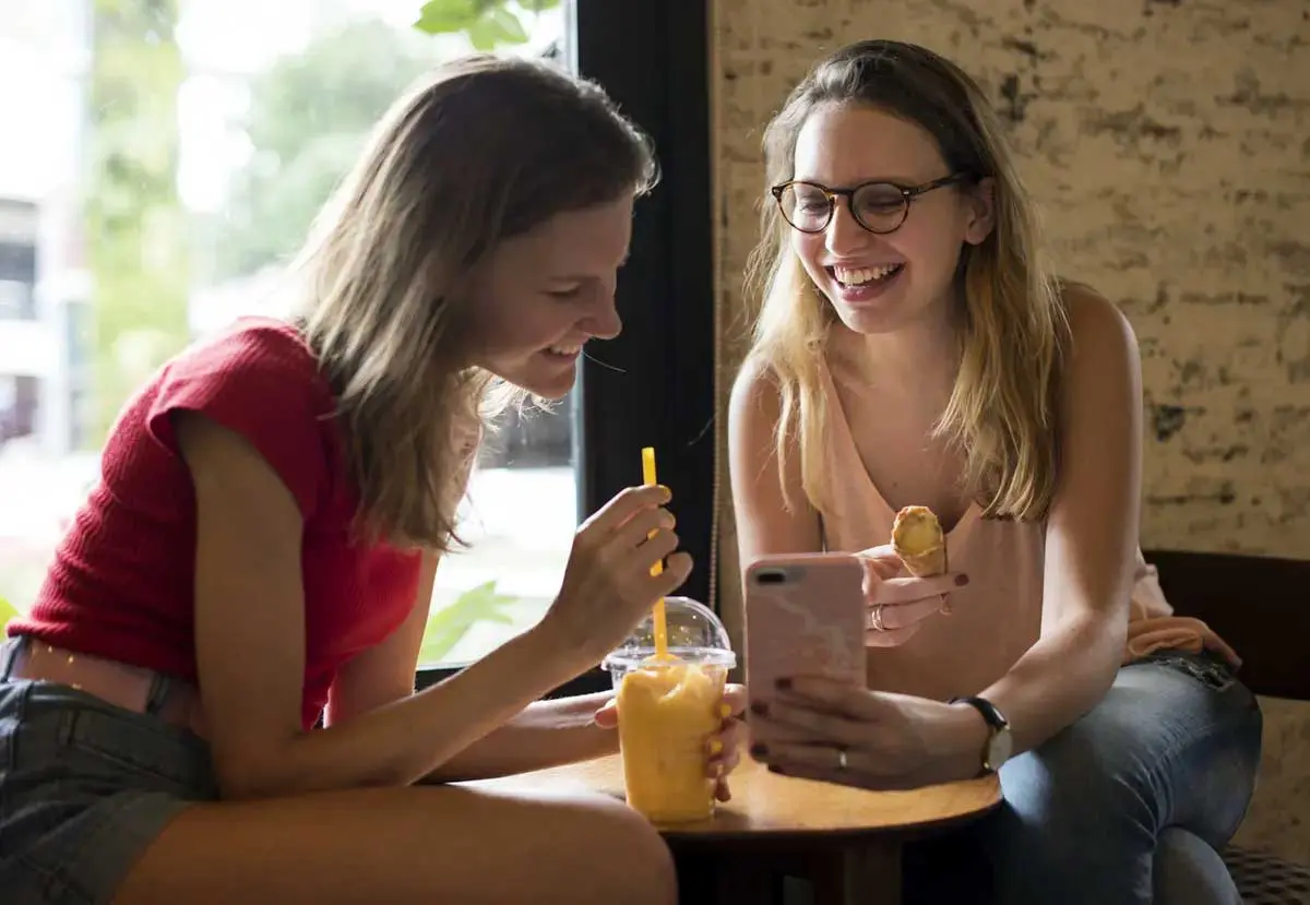 Two students looking at phone while enjoying a snack by the window